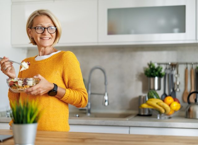 Mature woman eating salad at home.