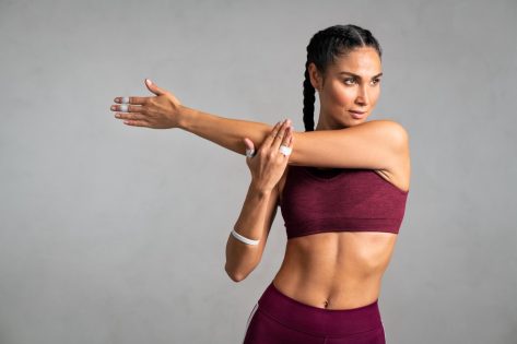 Portrait of fit middle aged woman doing arm stretching isolated on grey background