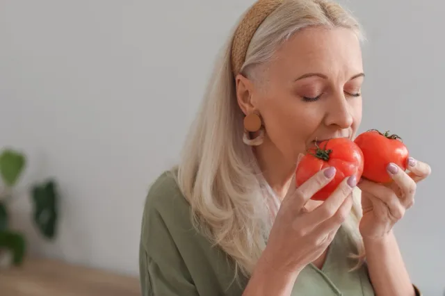 Mature woman with fresh tomatoes in kitchen, closeup.