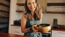 Healthy senior woman smiling happily while holding a wholesome buddha bowl. Mature woman serving herself a delicious vegan meal at home. Woman taking care of her aging body with a plant-based diet.