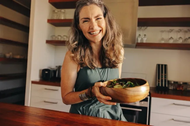 Healthy senior woman smiling happily while holding a wholesome buddha bowl. Mature woman serving herself a delicious vegan meal at home. Woman taking care of her aging body with a plant-based diet.