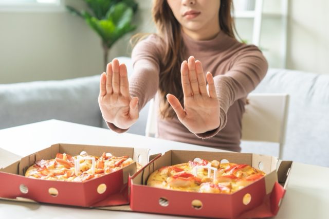 Diet concept, unhappy asian young woman, girl refusing to eat Pizza in box at home, hand pushing away, deny junk or fast food, fighting to keep it from getting fat. Healthy nutrition of weight loss.