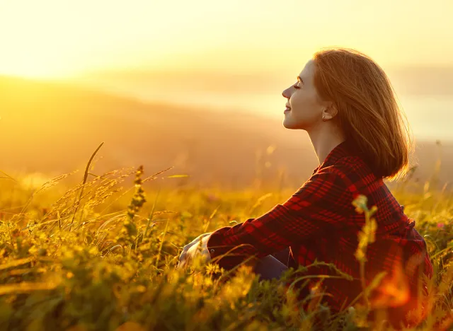 Woman sits with her back in the field and admires the sunset in the mountains