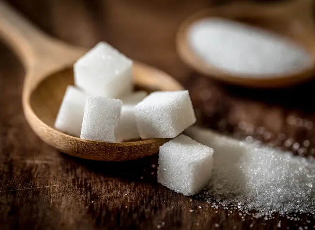 Close up sugar cubes and cane in wooden spoon on the table