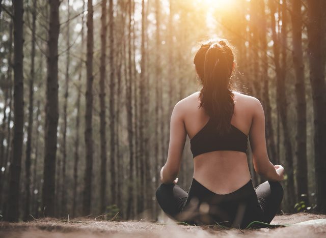 Back view of beautiful woman doing yoga pose in peaceful natural forest. Lifestyle and Meditation concept. Healthy and Mental training concept. Autumn seasonal and outdoors theme