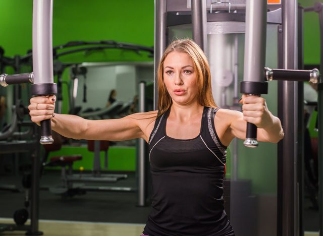 Woman doing fitness training on a butterfly machine with weights in a gym