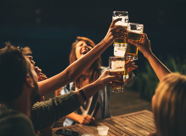 Group of friends drink beer on the terrace and toast during summer night