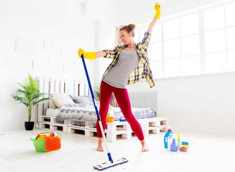 Woman in protective gloves is smiling and wiping dust using a spray and a duster