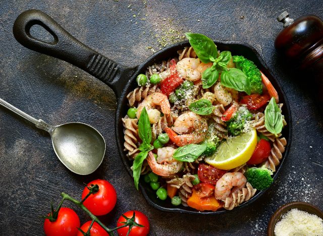 Whole wheat fusilli pasta with shrimps and vegetables in a skillet on a dark slate, stone, concrete or metal background.Top view.