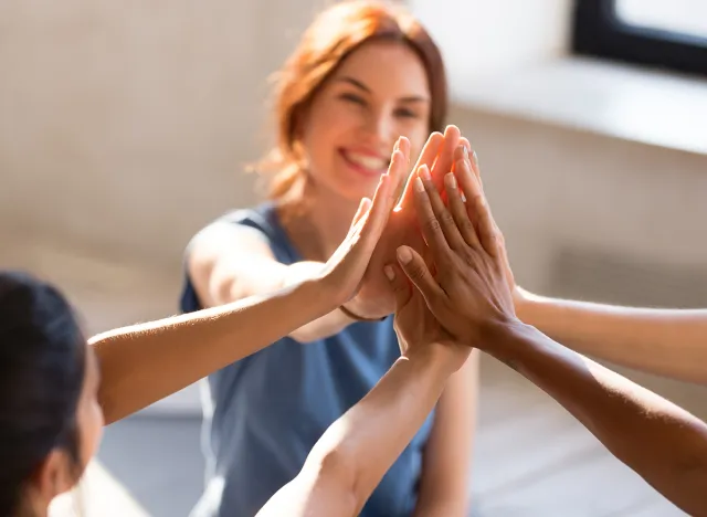 Cheerful diverse young girls sitting together in sports studio before starts training giving high five feel happy and healthy, close up focus on hands. Respect and trust, celebration and amity concept