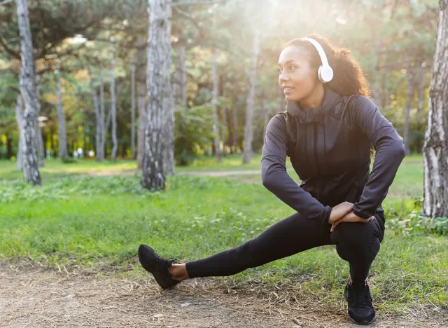 Photo of african american woman 20s wearing black tracksuit doing sports and stretching body in green park