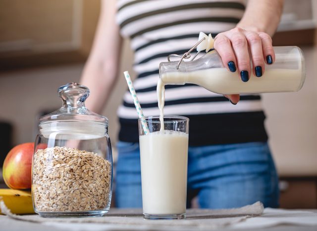 A woman pours organic oat milk from a bottle into a glass on a table in the kitchen. Diet healthy vegetarian product