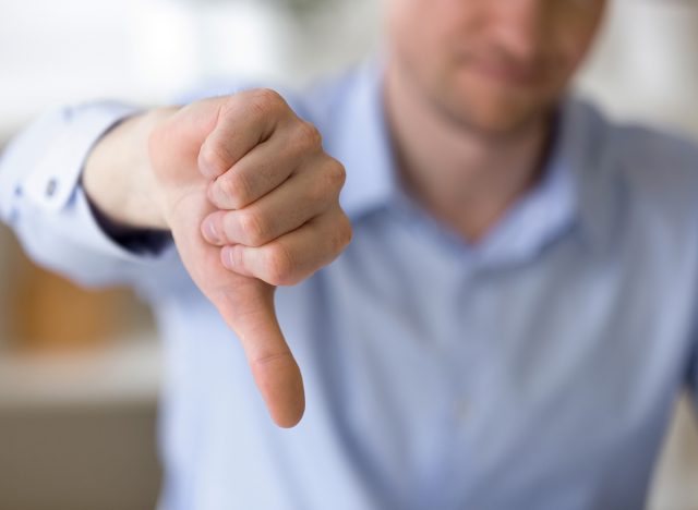 Close up of unrecognizable businessman with dissatisfied face showing negative sign, dislike with thumbs down, rejection concept at workplace, sign no, not approved, unhappy customer