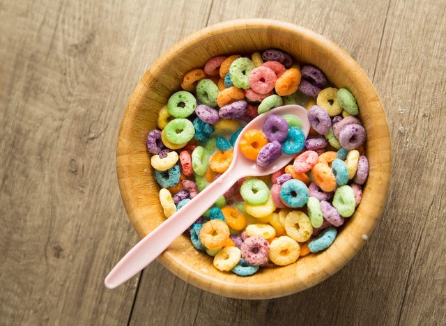 Fruity cereal in a bowl with milk and pink spoon in a wooden background