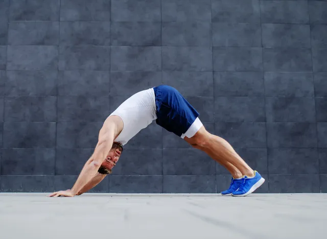 Side view of handsome fit muscular caucasian man doing inchworms exercise and looking at camera.