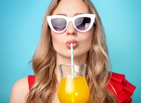 Beautiful woman drinks cocktail on blue background