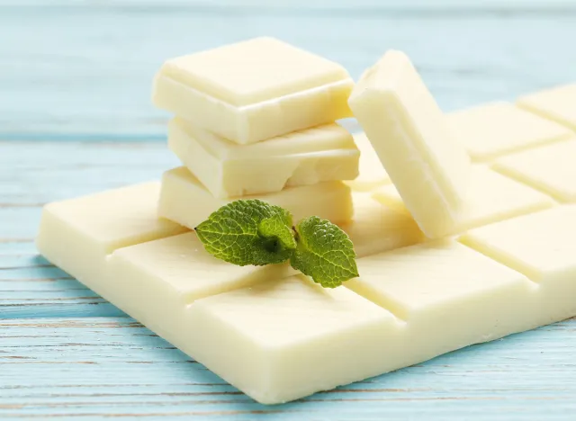 Bar and pieces of white chocolate on a blue wooden background. Top view. Place for text.