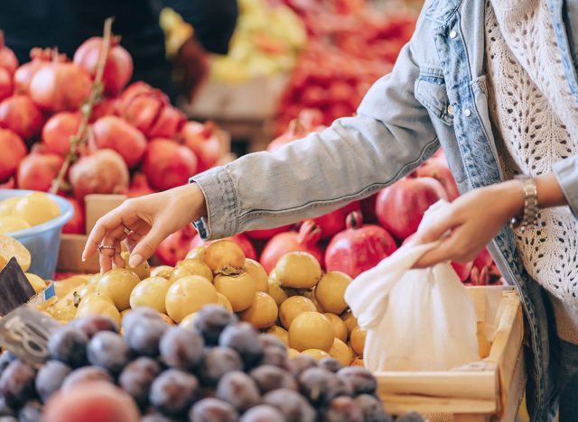 Female hands puts fruits and vegetables in cotton produce bag at food market. Reusable eco bag for shopping. Sustainable lifestyle. Eco friendly concept.