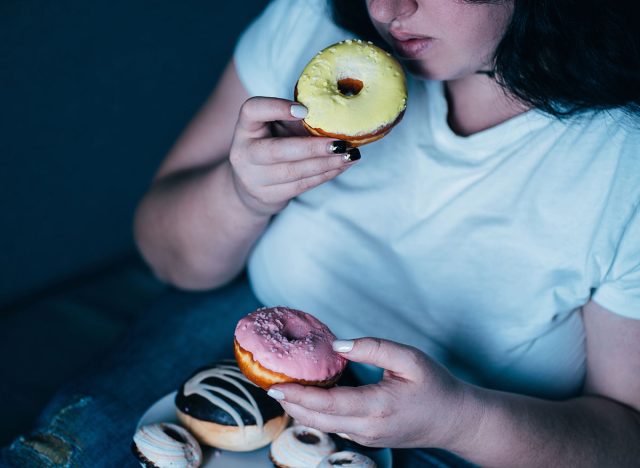 Emotional eating, mental disorder, depression, loneliness, stress. Lonely woman eating sweets and watching tv late in the night. Nerve food