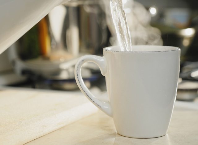 Close-up of hot boiled water is poured into a white ceramic cup on the table in the kitchen, brewing morning coffee