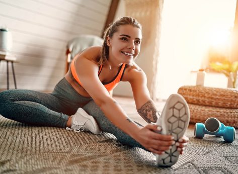 Athletic woman in sportswear doing fitness stretching exercises at home in the living room. Sport and recreation concept.
