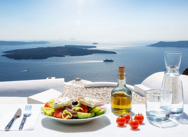 A Greek salad with olive oil and tomatoes in front of the a breathtaking view to the blue, Aegean sea as a concept of Greek food in summer time,