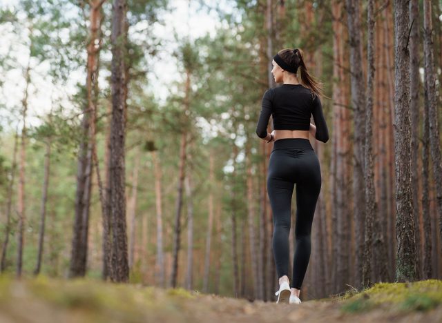 Young fitness woman running at forest trail. Sporty young girl running in the park in the summer morning. Teenager running in nature. Healthy lifestyle and relax concept. Weight loss content.