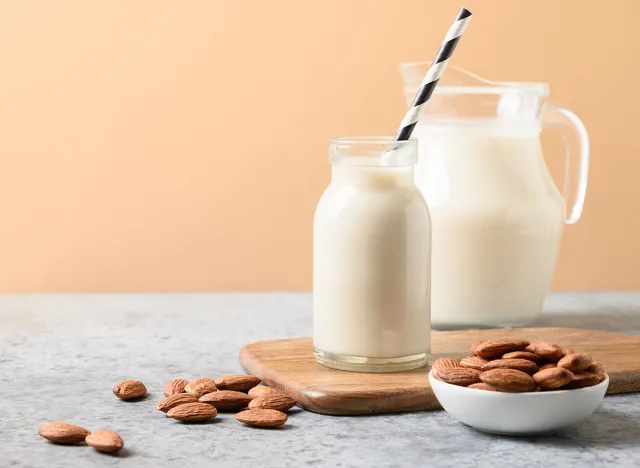 Almond milk in glass bottle and jug on beige background. Close up. Healthy vegan eating. Lack of cholesterol.