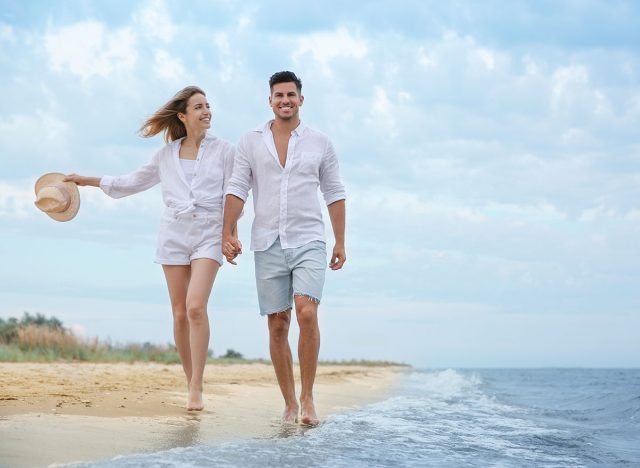 Happy couple having romantic walk on beach. Space for text