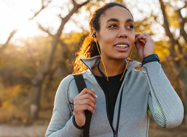 Happy african american sportswoman listening music with earphones while walking in park