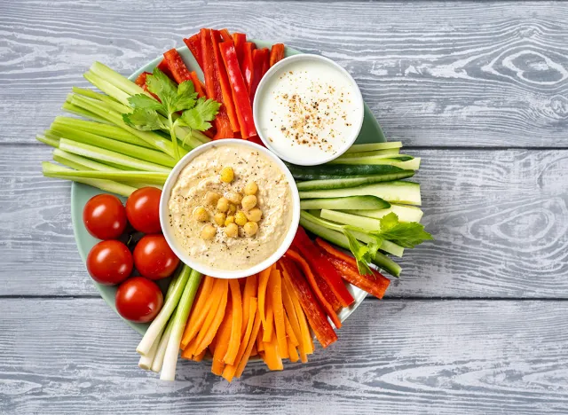 Plate of assorted colorful fresh vegetable sticks with hummus and yogurt dips on light blue background. Top view. Healthy raw vegetarian food enriched with vitamins and microelements