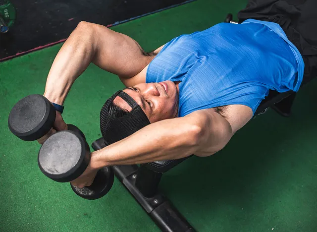 A fit asian man does a set of lying dumbbell tricep extensions. Working out Triceps and arms at the gym.