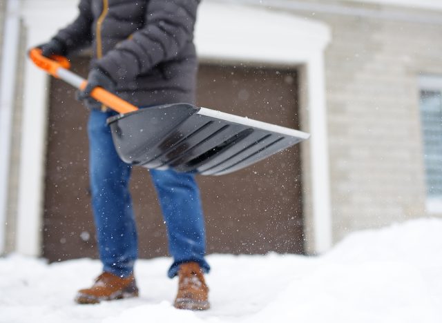 A mature man clean path near house from snow during strong blizzard. Person shoveling snow out of the driveway. Huge snowdrifts. Difficult situation in the city after a snow storm