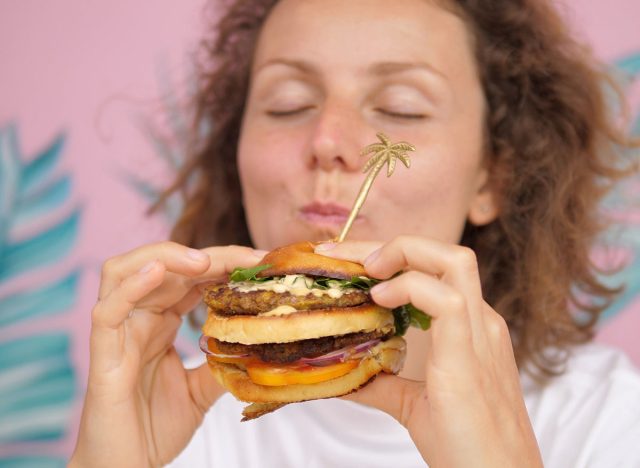 Close up of hungry Caucasian woman taking bite of double-decker vegan burger