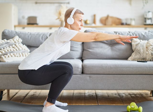 Senior woman stretching, online training in living room. Balancing yoga exercise. Exercising for emotional and spiritual health. Well-being, wellness for retired female. Domestic yoga practice