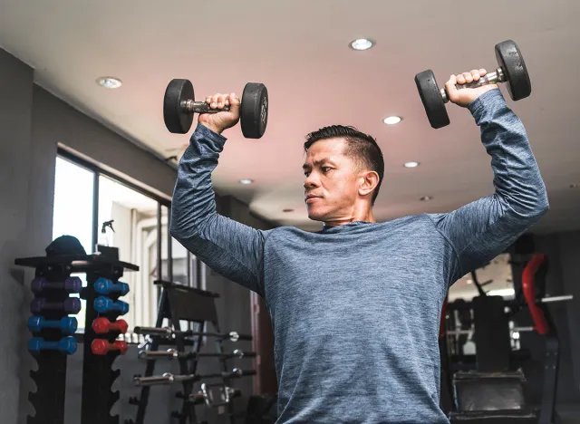 A health conscious man in his early 40s doing seated dumbbell presses. Maintaining a healthy physique in middle age.