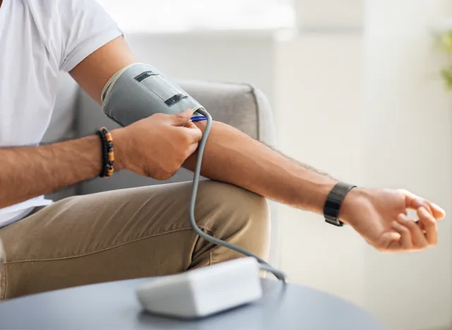 Closeup of unrecognizable male patient using modern tonometer at home, panorama with copy space. Cropped of middle-eastern man measuring his blood pressure, making self checkup