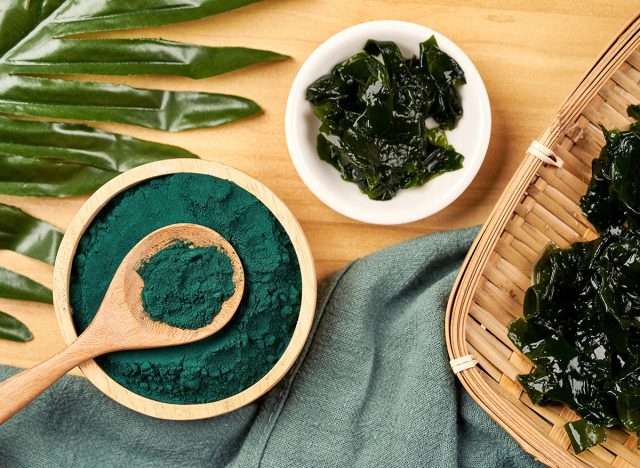 Top view laminaria or kelp seaweed and spirulina powder in wood bowl and spoon background. flat lay spirulina powder with konbu and alga food on wood table background.