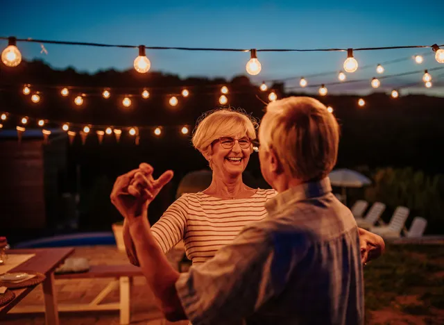 Beautiful senior couple dancing together in their backyard decorated with lamps