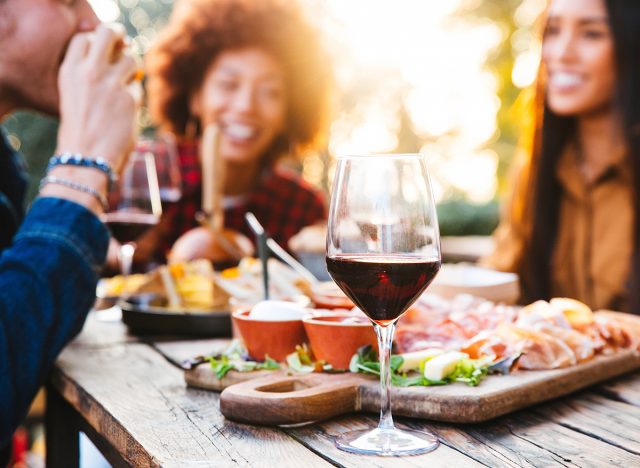 Happy family having barbecue party in backyard - Young friends celebrating at dinner drinking red wine at sunset - Focus on wine glass