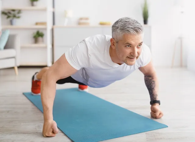 Strong senior man making strength workout, doing push ups on sports mat, exercising at home, copy space. Sporty elderly man training his body, leading active lifestyle