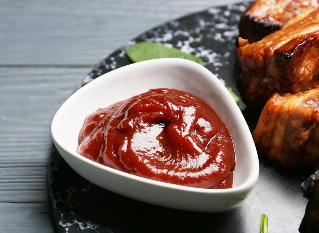 Bowl with tasty barbecue sauce and roasted pork on dark wooden background