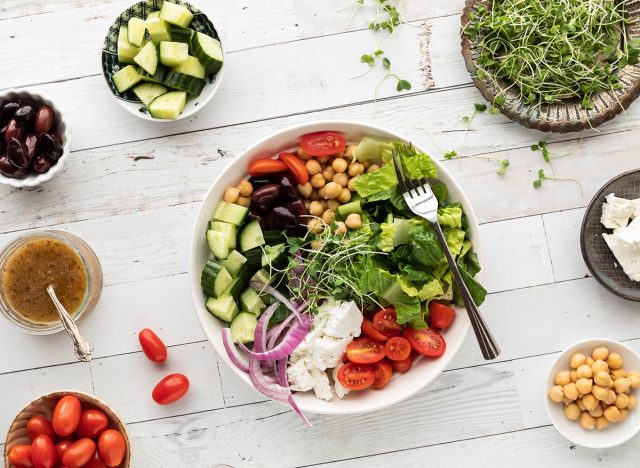 Top down view of a Greek salad bowl with separate bowls of the ingredients.