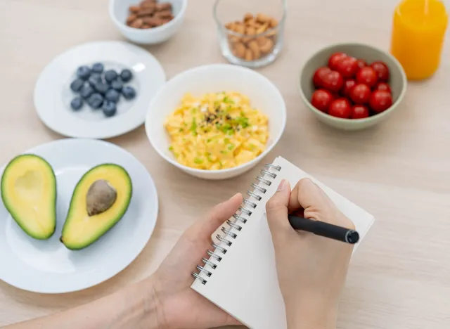 Diet, Dieting hand of asian young woman, girl write diet plan nutrition on table is different food ingredients in the green. Nutritionist of healthy, nutrition of weight loss, health care people.