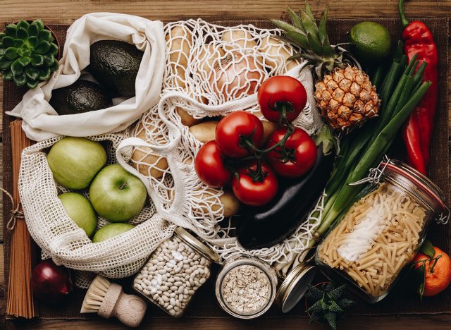 Zero waste food shopping. Fruit and vegetables in cotton bags, pasta, cereals and legumes in glass jars, herbs and spices on wooden background. Healthy food, clean eating, eco friendly, no plastic con