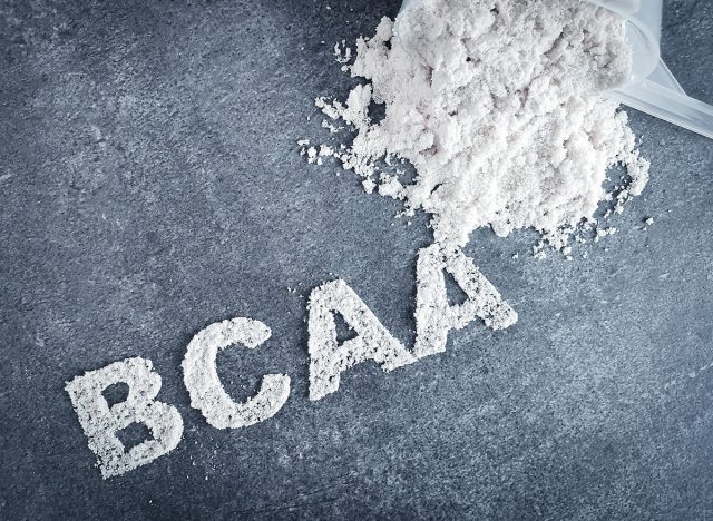 BCAA branched chain amino acid text made of powder on grey background with scoop and dumbbell used by bodybuilders before workout as a pre-workout supplementation