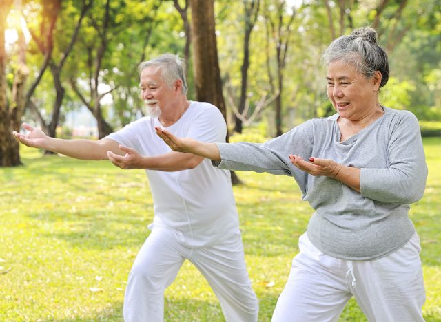 Asian senior couple practice yoga excercise, tai chi tranining, stretching and meditation together with relaxation for healthy in park outdoor after retirement. Happy elderly outdoor lifestyle concept