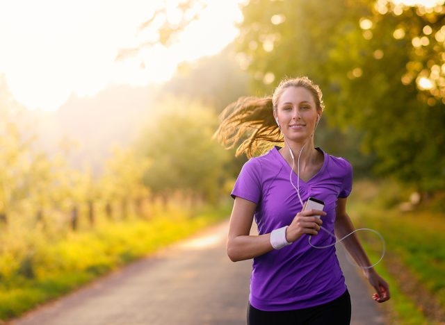 Woman listening to music on her earplugs and MP3 player while jogging along a country road in a healthy lifestyle, exercise and fitness concept