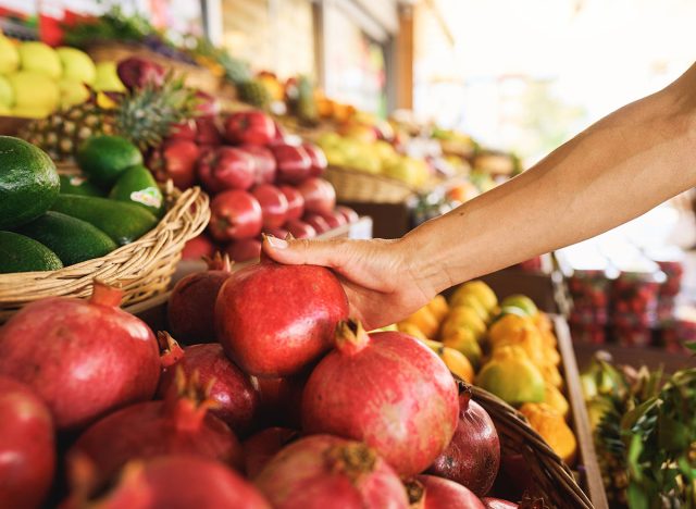 Woman choosing pomegranate among many others while having great food shopping at the local food market. Stock photo. High quality photo