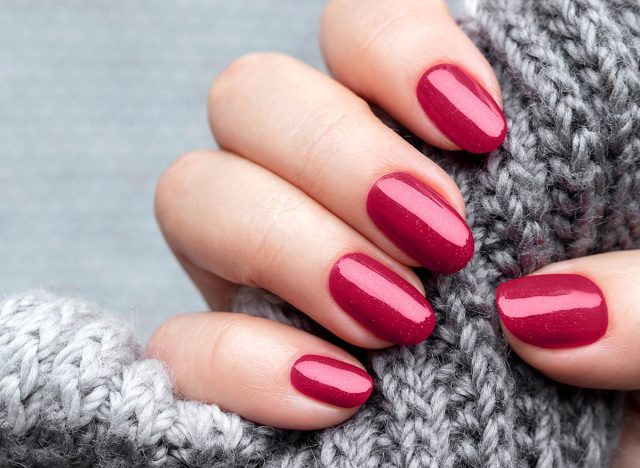 Female hand with knitted scarf and beautiful manicure - viva magenta, burgundy glittered nails